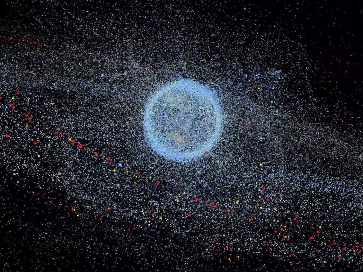 An image of the Earth appears on a black background. The Earth is swarmed by satellites and space debris that form a glowing, granular cloud around it.